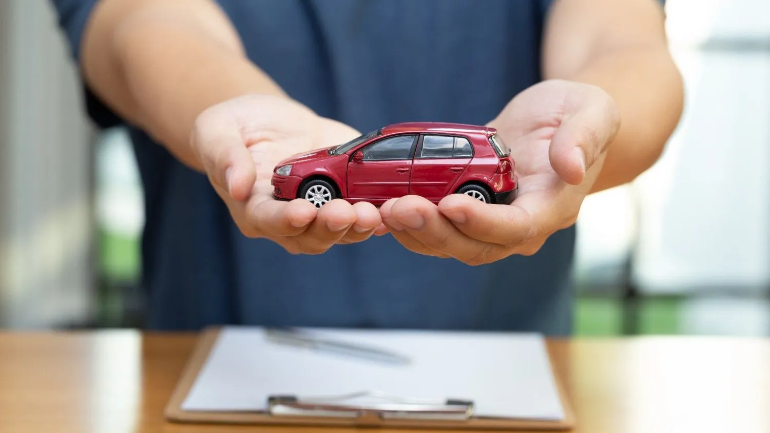 Hands holding a small red car above a policy form
